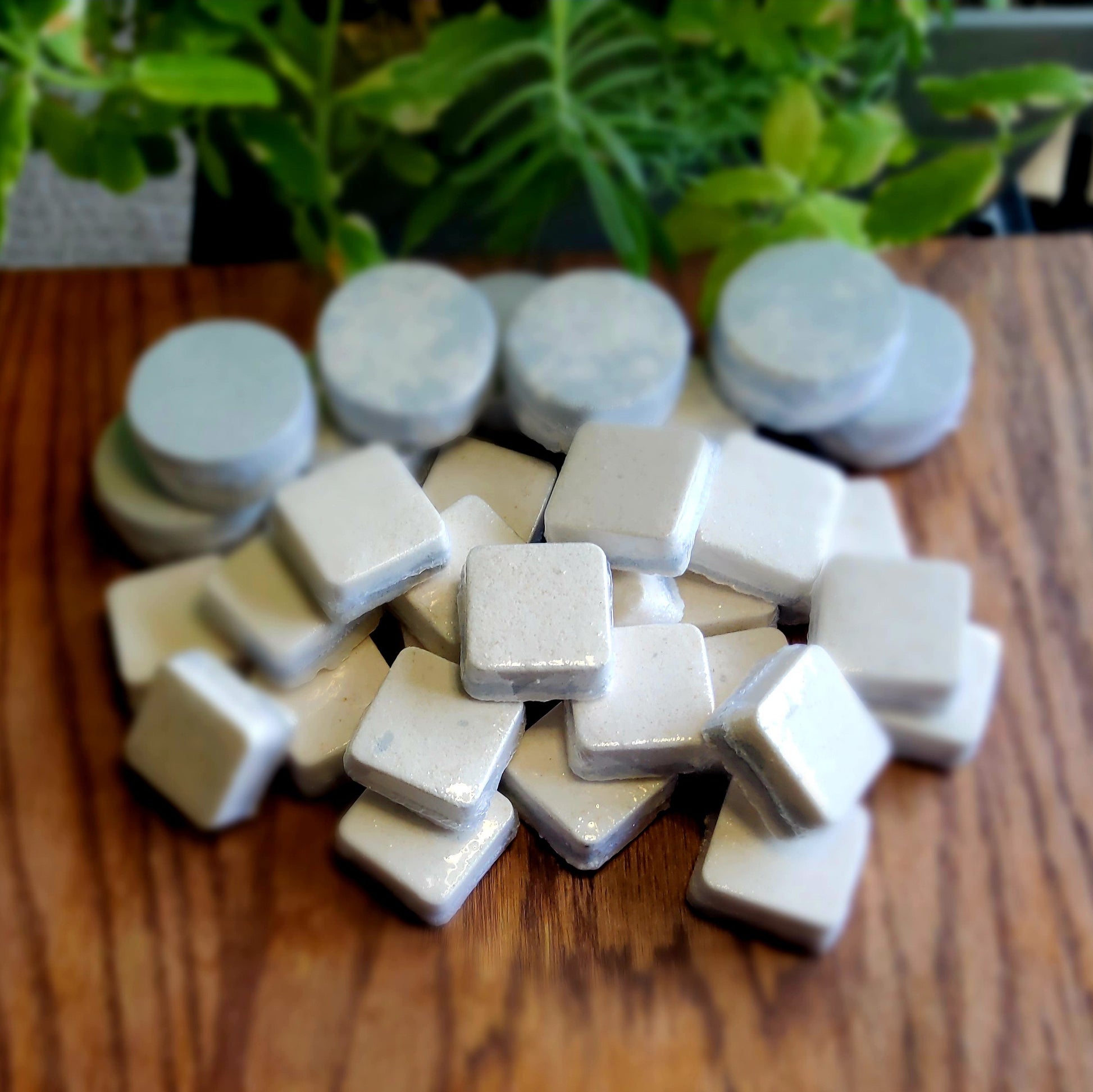Square-shaped shower steamers colored with swirled colors of grey and peach mica handmade in small batches by Gothic & Ivy. With a grey planter behind them showcasing three different kinds of mint.
