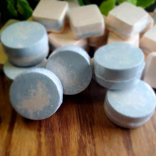 One inch round shower steamers colored with swirled colors of grey and peach mica handmade in small batches by Gothic & Ivy. With a grey planter behind them showcasing three different kinds of mint.