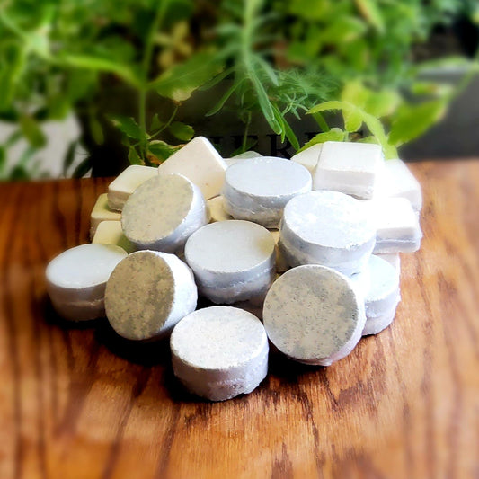 One inch round shower steamers colored with swirled colors of grey and peach mica handmade in small batches by Gothic & Ivy. With a grey planter behind them showcasing three different kinds of mint.