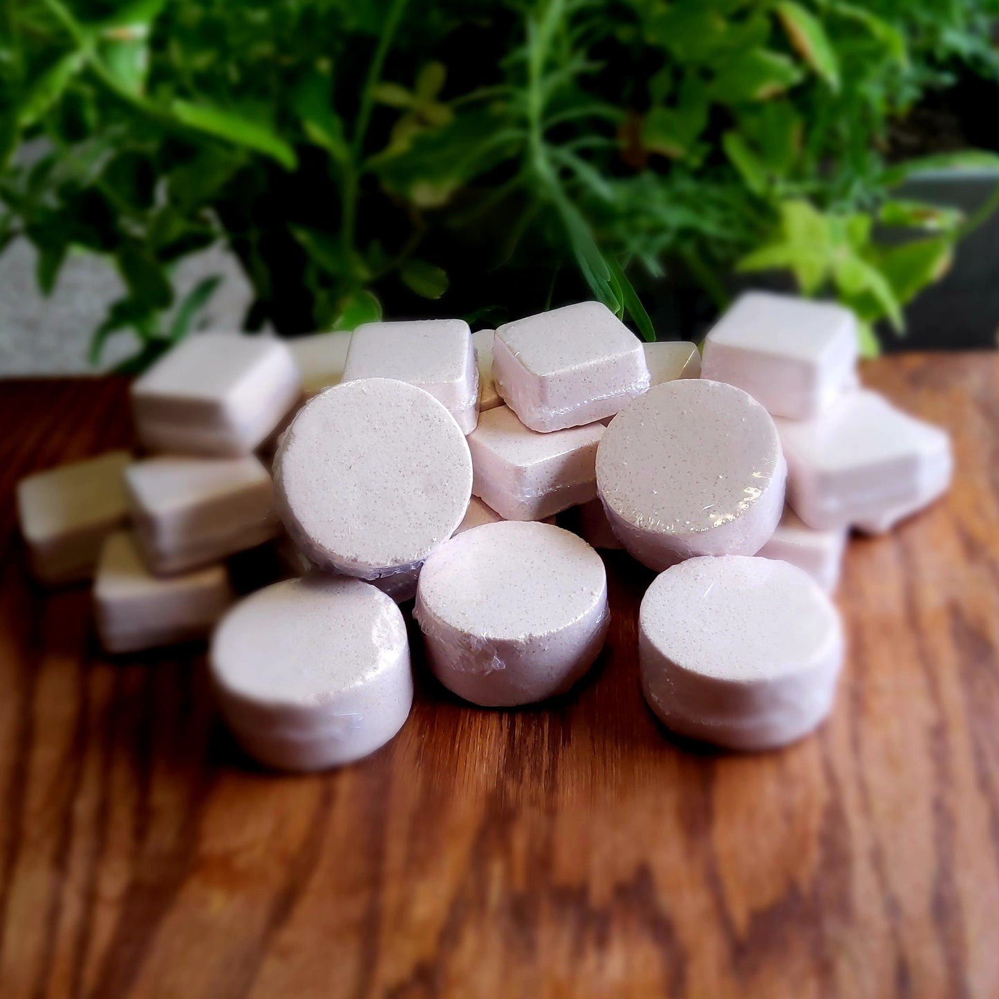 One inch round shower steamers colored with a sandstone copper with flecks of orange glitter handmade in small batches by Gothic & Ivy. With a grey planter behind them showcasing three different kinds of mint.