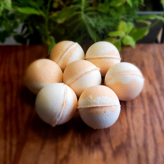 Swirling pattern of orange and white bath bombs, colored with natural mica handcrafted with care by Gothic & Ivy, arranged in front of a grey planter containing three varieties of freshly growing mint.