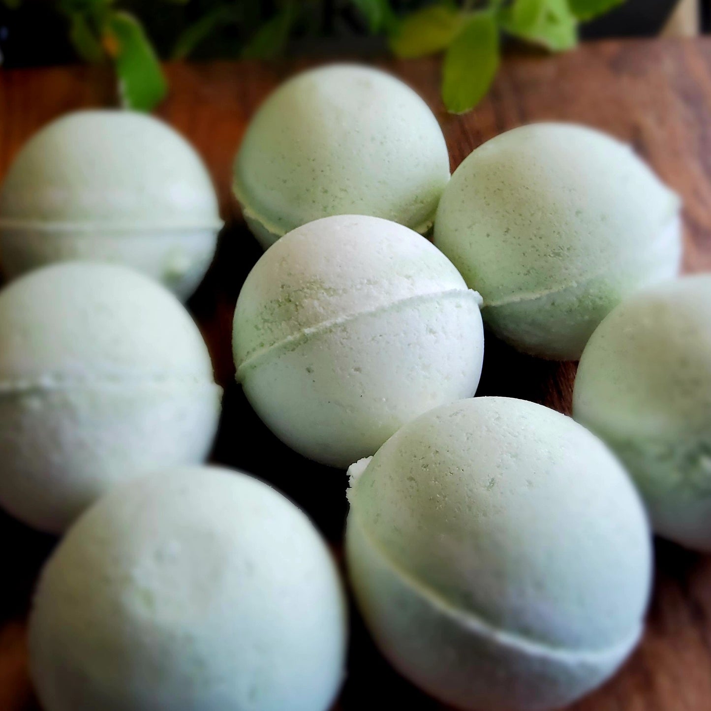 Swirling pattern of pale green and white bath bombs, colored with natural mica handcrafted with care by Gothic & Ivy, arranged in front of a grey planter containing three varieties of freshly growing mint.